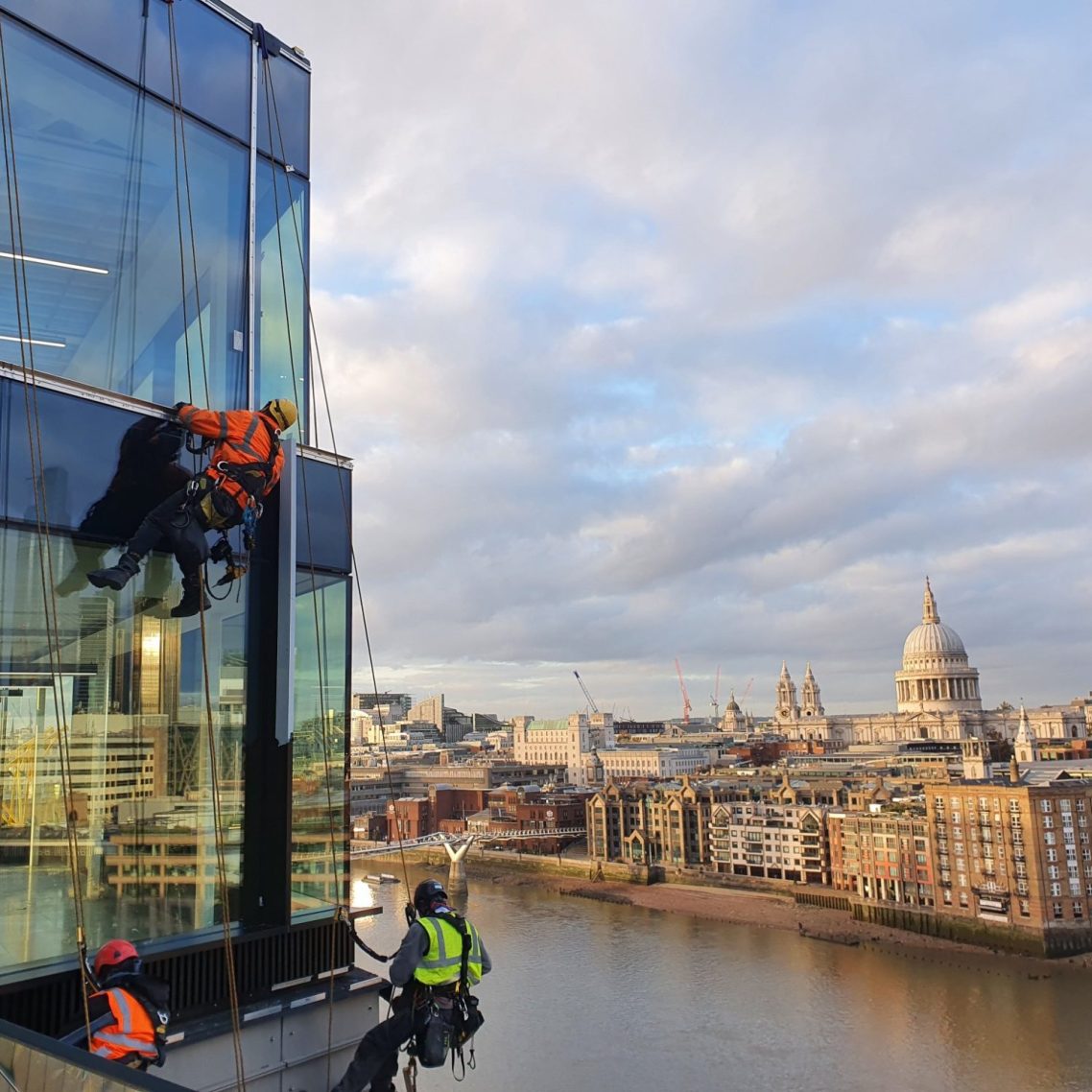 Rope access St Paul's London Workers abseiling down a glass building with St Paul's Cathedral and the river Thames in the background.